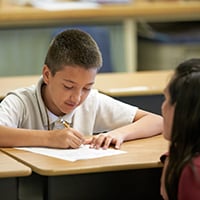 A teacher in front of a student at their desk who is writing