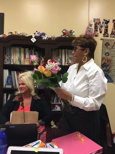 A teacher standing in front of a room receiving flowers