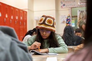 Photo a middle school student wearing a crochet bucket hat working on a work book at her desk