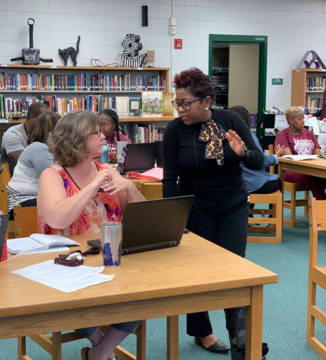 an ANet coach standing and talking to a teacher sitting down at a table